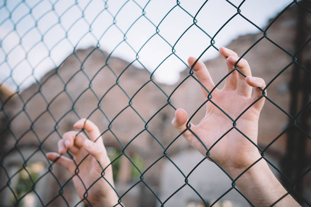 Refugee hands keeping metal fence mesh - Photo, Image