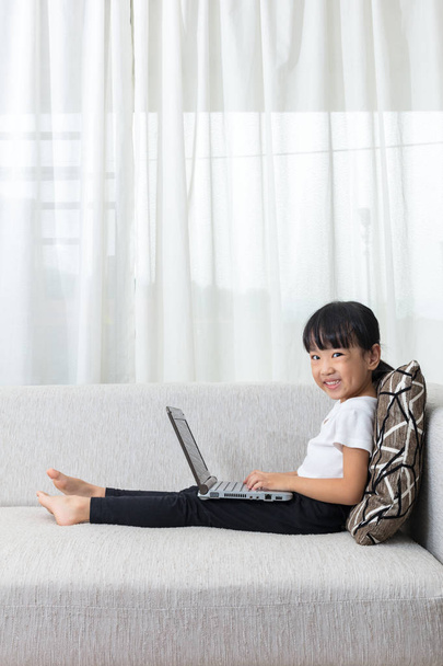 Happy Asian Chinese little girl lying on sofa with laptop - Foto, immagini
