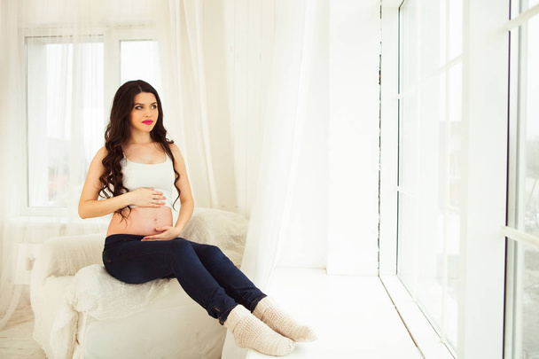Jovem mulher grávida feliz sentado na janela em sua casa
 - Foto, Imagem