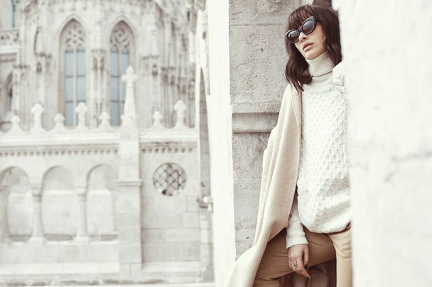Pretty young model female in light pullover and sunglasses with great architecture on background - Foto, Bild