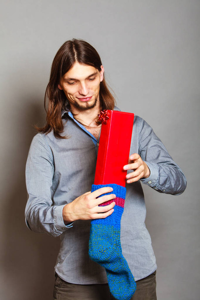 Guy putting wrapped gift in knitted christmas sock - Foto, Imagem