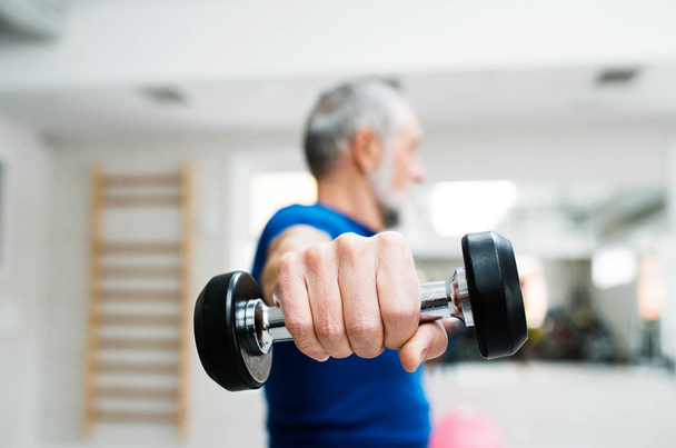 Senior man in gym working out with weights. - 写真・画像