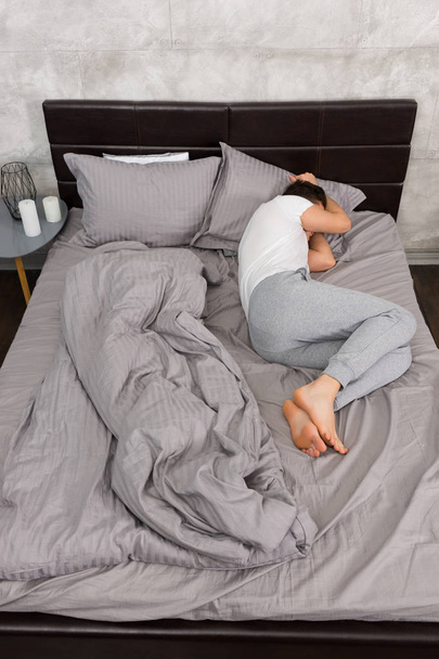 Young tired man in pajama sleeping without blanket in stylish be - 写真・画像