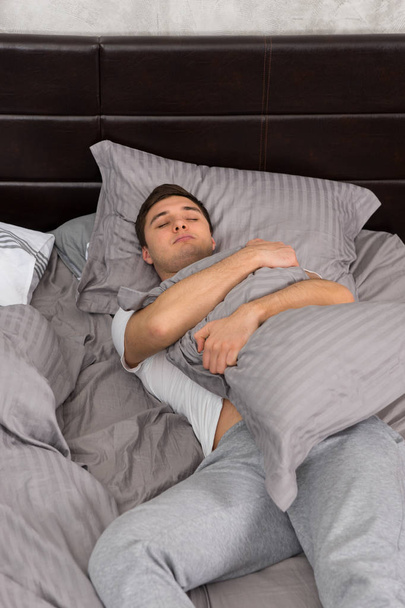 Handsome young tired man in pajama sleeping alone without blanke - Фото, изображение