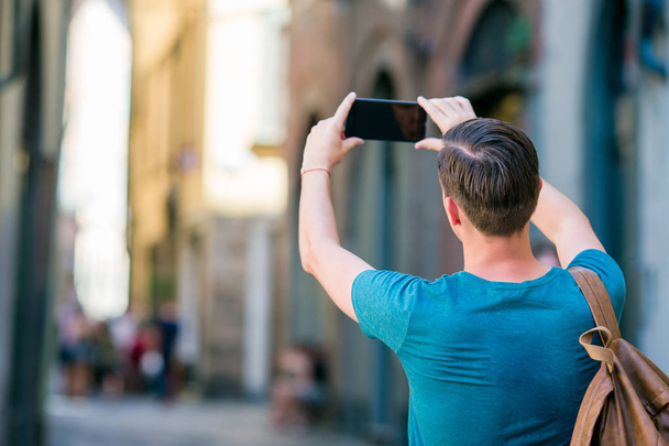 Uomo turistico che scatta foto con lo smartphone in mano passeggiando per le strette strade italiane in Europa. Giovane ragazzo urbano in vacanza esplorando la città europea
 - Foto, immagini