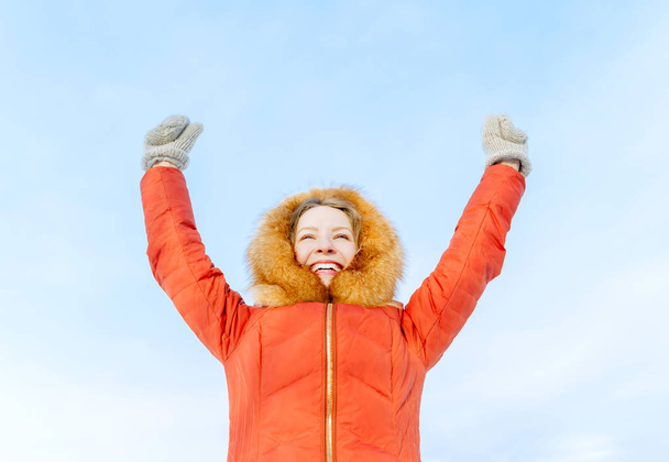 Outdoor portrait of a smiling girl in winter down jacket, raise their hands against the blue sky - Foto, immagini