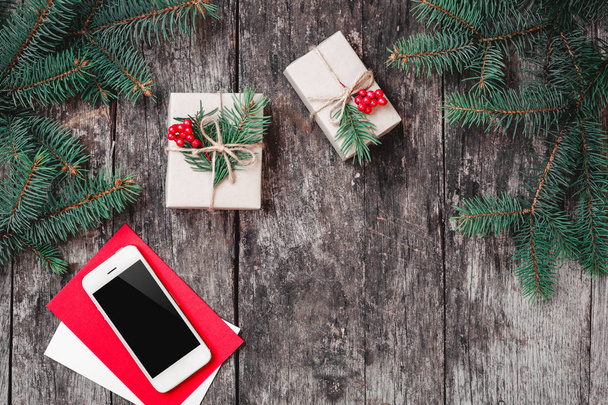 Vánoční pozadí s smartphone, vánoční dárek, větve jedle na dřevěné pozadí s větvemi jedlí. Vánoce a šťastný nový rok složení. Plochá ležel, horní pohled - Fotografie, Obrázek