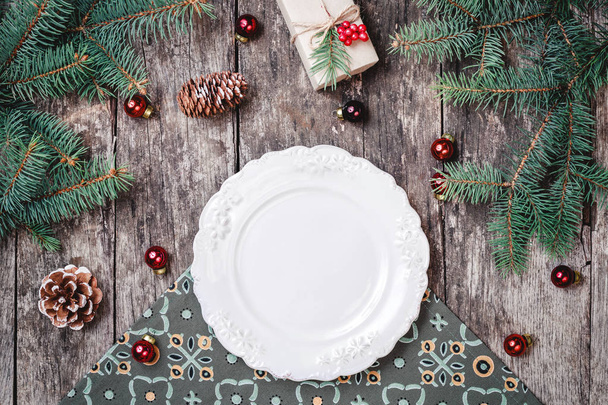 Christmas plate on wooden holiday background with gift, pine cones, red decorations, Fir branches. Xmas and Happy New Year composition. Flat lay, top view - Photo, Image