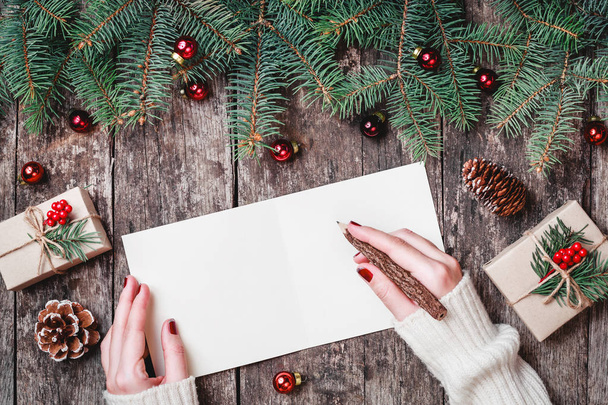 Female hand writing and reading a letter to Santa on wooden background with Christmas gifts, Fir branches and candy. Xmas and Happy New Year composition. Flat lay, top view - Foto, Bild
