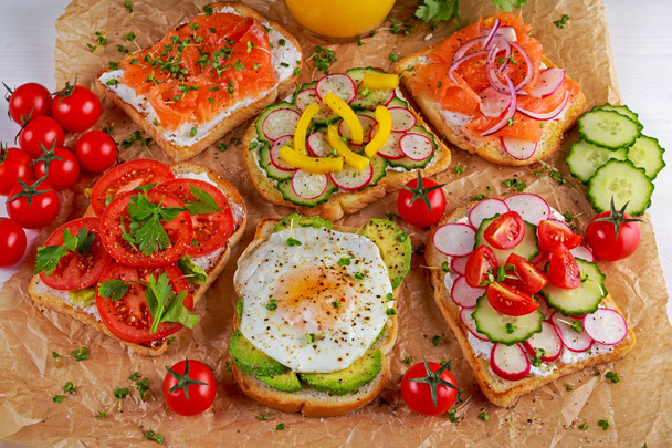 Scala aan vegetarische toast sandwiches met zalm, raddish, tomaten, komkommer, avocado, gebakken ei en paprika - Foto, afbeelding