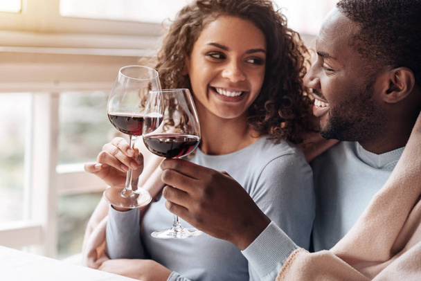 Positive African American couple holding wineglasses in the restaurant - 写真・画像