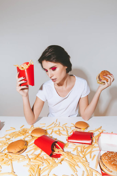 Pretty young woman holding french fries and burger - Foto, immagini