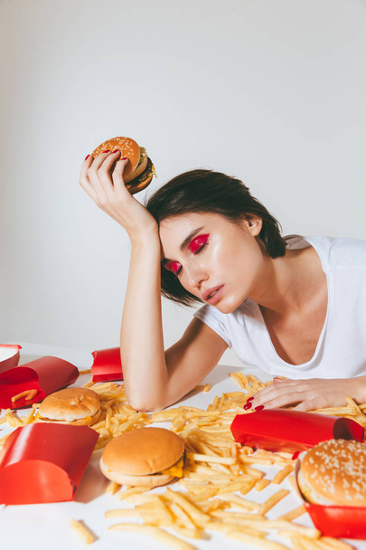 Exhausted sleepy woman sitting at the table with fast food - Фото, изображение