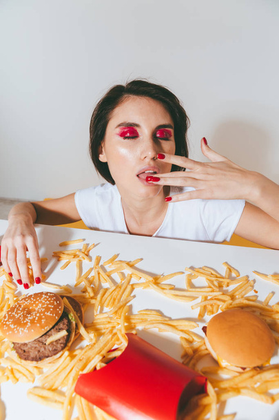 Sensual young woman licking her finger after eating fast food - Photo, image