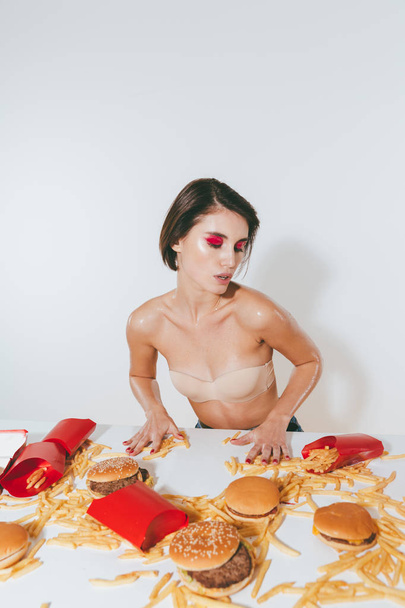 Sensual young woman sitting at the table with fast food - Fotó, kép