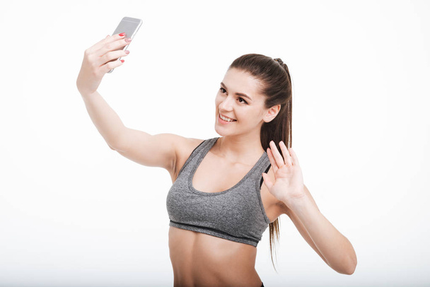 Happy smiling fitness woman waving at her mobile phone - Foto, afbeelding