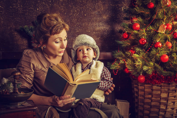 Mother reads to his son the book near a Christmas tree. - Foto, Imagen