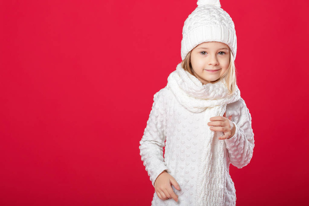 little smiling blonde girl in a white hat and scarf on red backg - Φωτογραφία, εικόνα