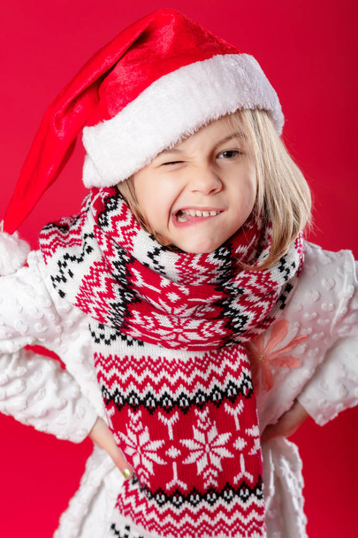 little girl in santa hat and scarf on red background - Фото, зображення