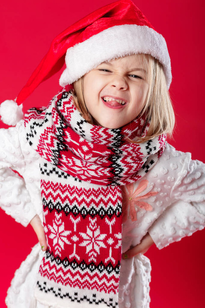 little girl in santa hat and scarf on red background - Фото, зображення