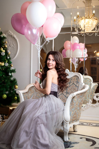 beautiful young woman in luxury evening dress with air balloons over christmas background - Фото, изображение