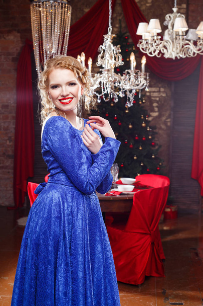 Pretty cheerful young lady in a blue evening dress over christmas background - Фото, зображення
