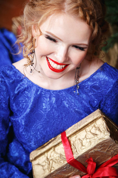 Pretty cheerful young lady in a blue evening dress over christmas background - Fotoğraf, Görsel