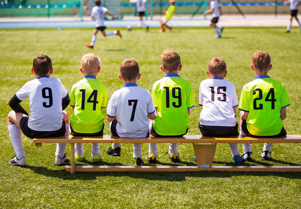 Αγόρια που παίζουν ποδόσφαιρο. Νέοι ποδοσφαιριστές. Ομάδα νέων ποδοσφαίρου κάθεται στο ξύλινο πάγκο. Αγώνα ποδοσφαίρου για παιδιά. Νεαρά αγόρια που παίζουν αγώνα ποδοσφαίρου τουρνουά. Νεολαία Ποδόσφαιρο Club ποδοσφαιριστές - Φωτογραφία, εικόνα