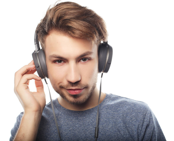 Handsome young man wearing headphones and smiling while standing - Фото, зображення