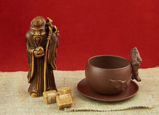 Натюрморт с статуэтка Бога чая, чашки и куски o - Фото, изображение