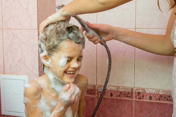 Мама моет мыло и шампунь в душе с семилетней дочерью
 - Фото, изображение