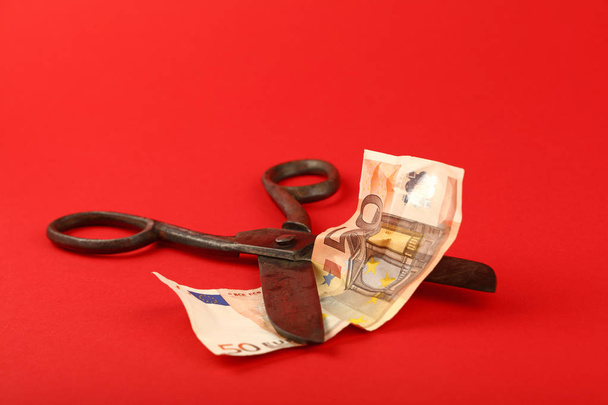 Το Ψαλίδι κόβει τραπεζογραμματίου ευρώ σε κόκκινο φόντο - Φωτογραφία, εικόνα