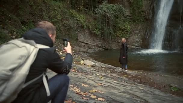Mladý muž pořizování fotografii dívky před zpomalené krásný vodopád - Záběry, video