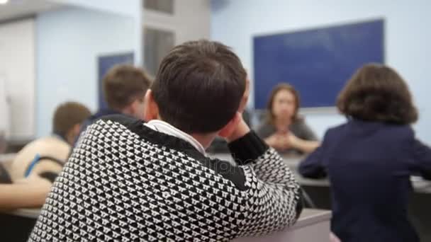 Klassenkameraden in der Schule - Junge sitzt am Tisch und schaut, während der Lehrer die Lektion erklärt - Filmmaterial, Video