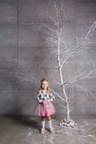Pretty girl child 3 years old in a pink dress. in holiday gray room with tree. - Foto, Bild