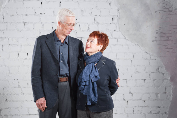 Happy smiling old couple standing cuddling together isolated on white brick background. copy space. - Photo, image
