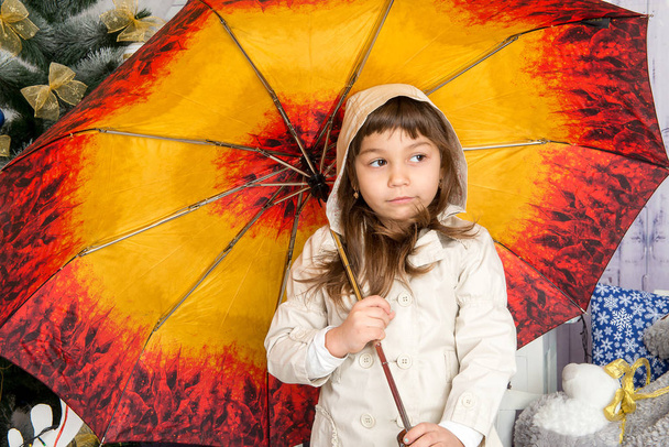 The child, a girl in a beige coat hiding under an umbrella from the rain fall. - Photo, Image