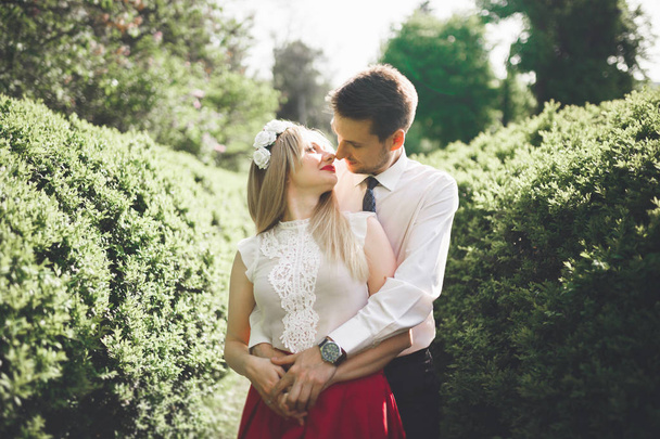 Young beautiful couple kissing and hugging near trees with blossom in summer park - Fotoğraf, Görsel