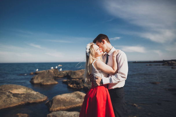 Romantic loving couple posing on stones near sea, blue sky - Valokuva, kuva