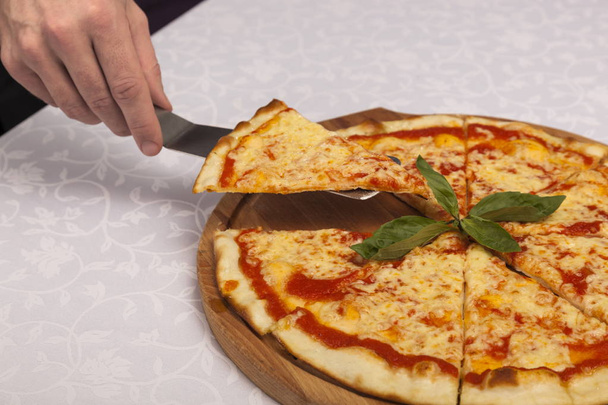 Pala de mano toma una rebanada de pizza sobre fondo blanco
 - Foto, imagen