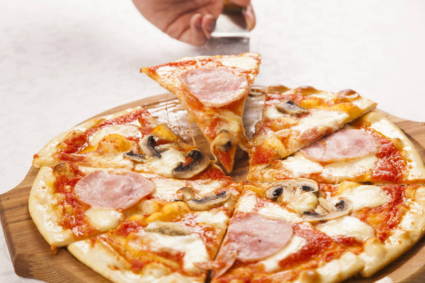 Hand Schaufel nimmt ein Stück Pizza auf weißem Hintergrund - Foto, Bild
