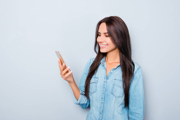 Lächelndes Mädchen liest Nachricht auf Handy auf grauem Hintergrund - Foto, Bild