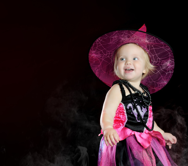 Halloween baby witch with a carved pumpkin over black background - 写真・画像