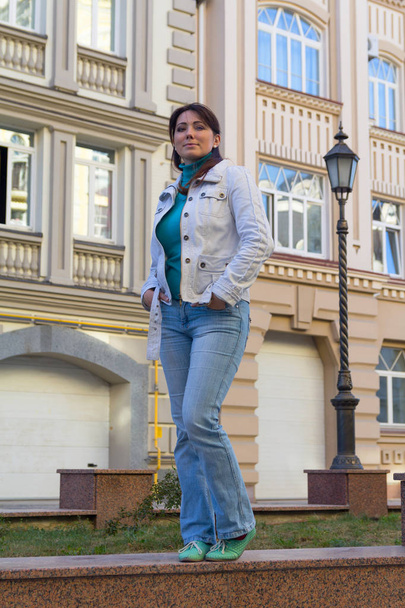 Όμορφη γυναίκα σε ένα λευκό σακάκι με φόντο ένα σπίτι. ΠΕΟ - Φωτογραφία, εικόνα
