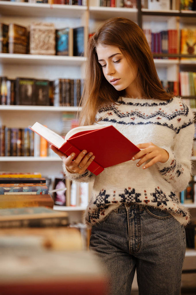 Young pretty woman standing and reading book in library - Photo, Image