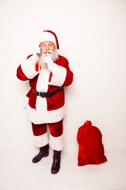 Shh! Santa Claus with christmas bag talking on phone - Foto, afbeelding
