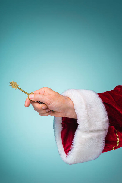 Hand of Santa Claus holding the key on blue background - 写真・画像