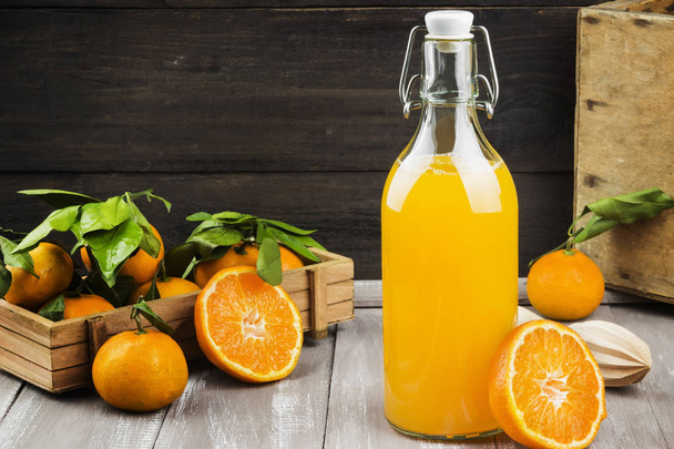 Bottle of tangerine juice and fresh fruit on a wooden background - Zdjęcie, obraz