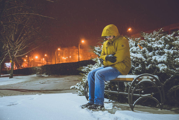 Man zit op een bankje in koude winternacht - Foto, afbeelding