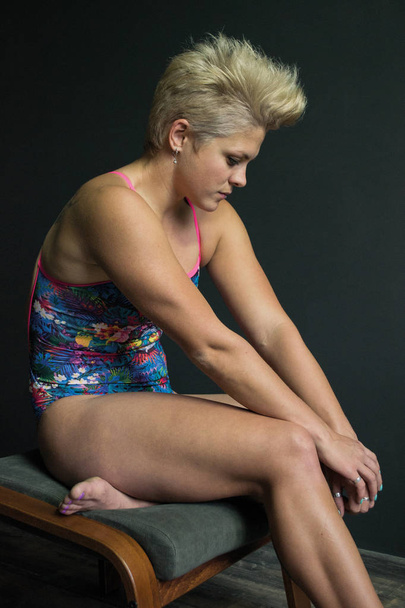 Foto Sport Mädchen sitzt auf einem Hocker im Badeanzug grauen Hintergrund - Foto, Bild